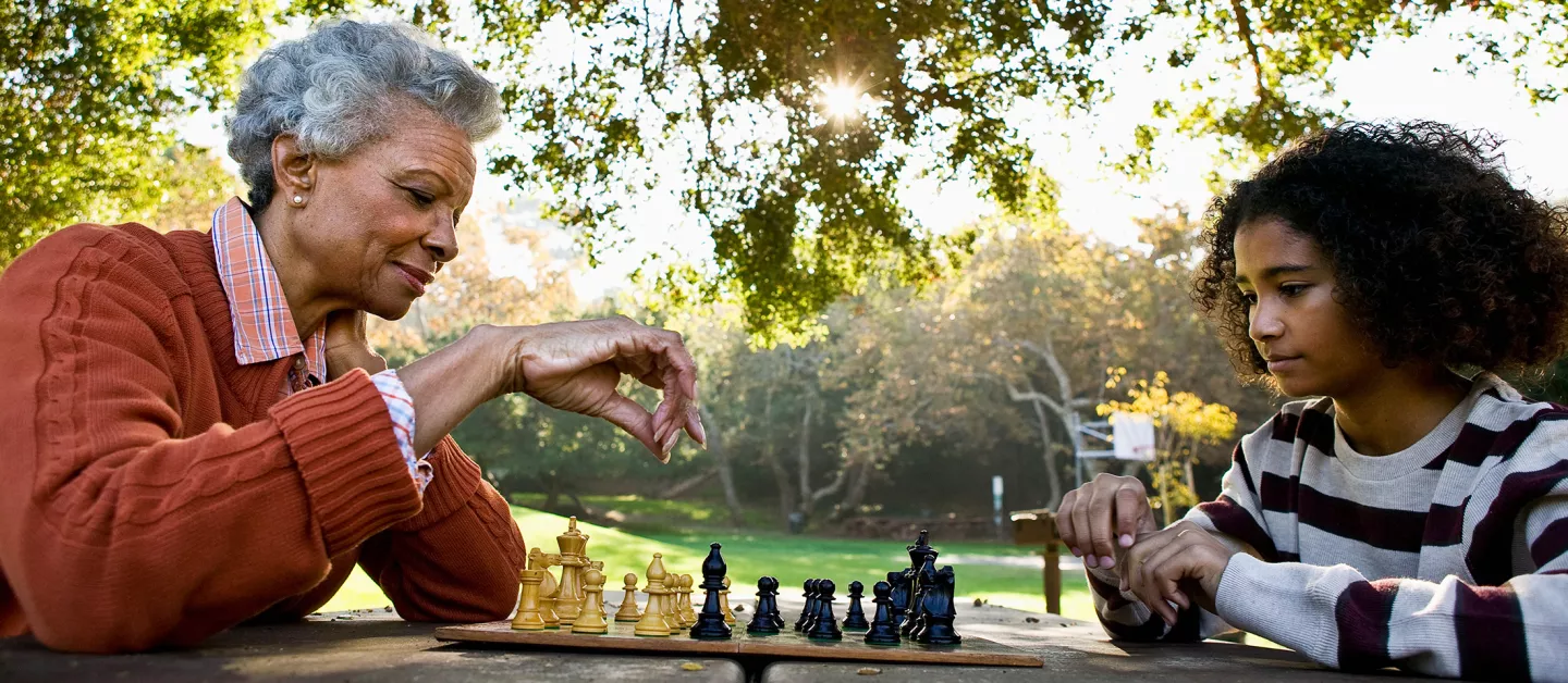 Older woman playing chess with granddaughter.