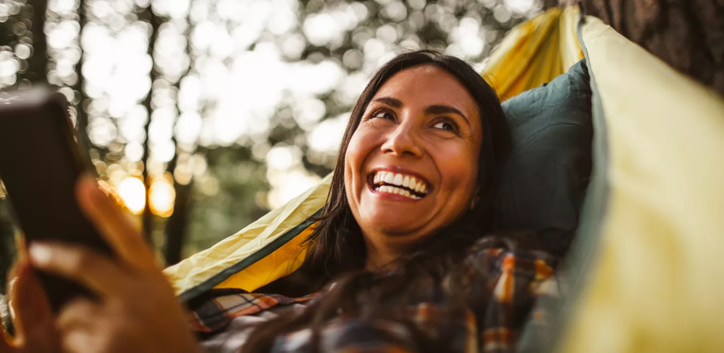 Woman using a smart phone while lying in a hammock in the forest.