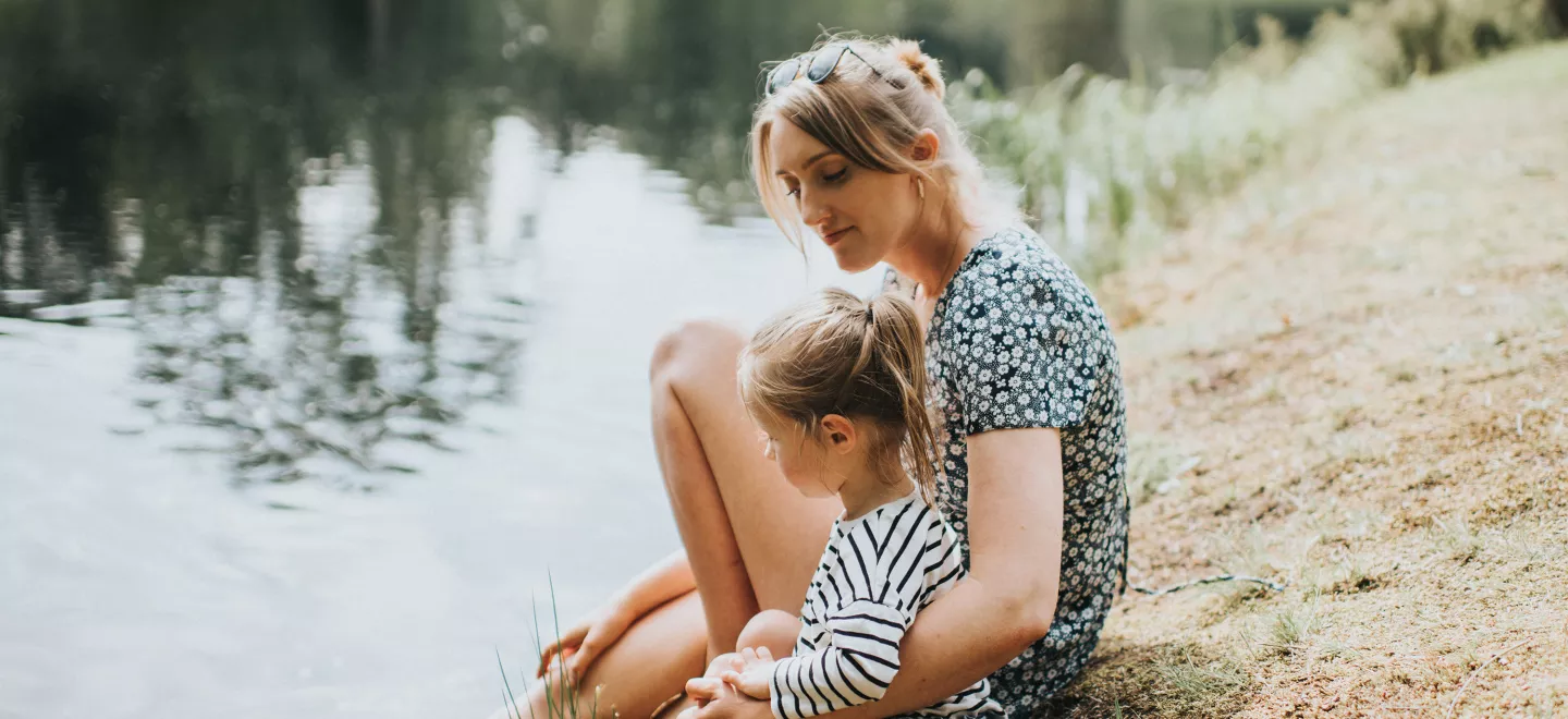 A woman and her daughter sitting on the edge of a lake
