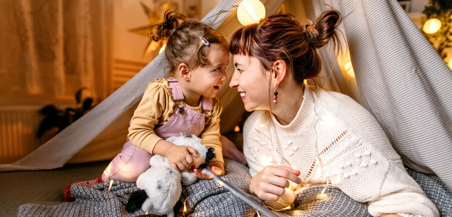 Mother and daughter are having fun reading a book under the illuminated tent in the bedroom.