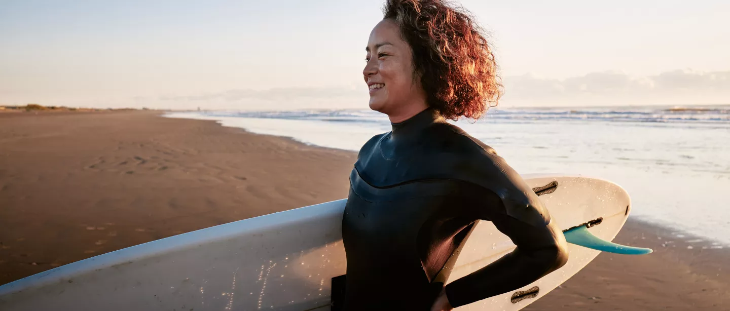 Side view portrait of a woman standing in the surf with a surfboard under her arm. 