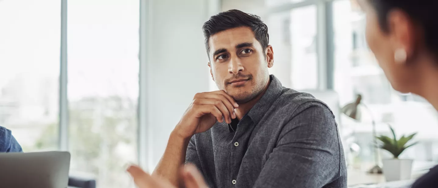 Young professional in conversation seated at table in sunny office