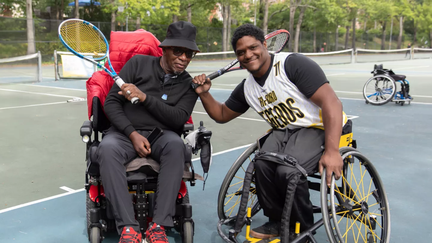 Two wheelchair tennis players smiling on a sunny tennis court