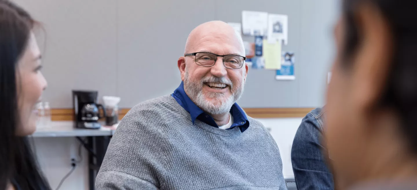 Gentleman and others gathered around a table smiling in a group discussion