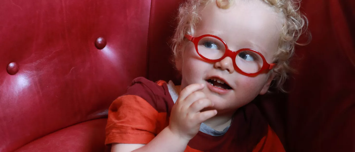 A little girl wearing red glasses sitting on a red couch