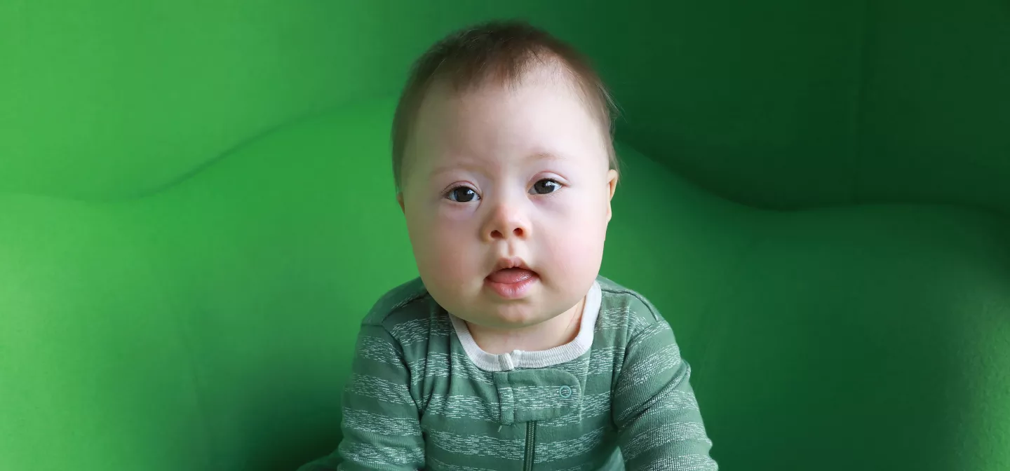 A young baby sitting in front of a green wall