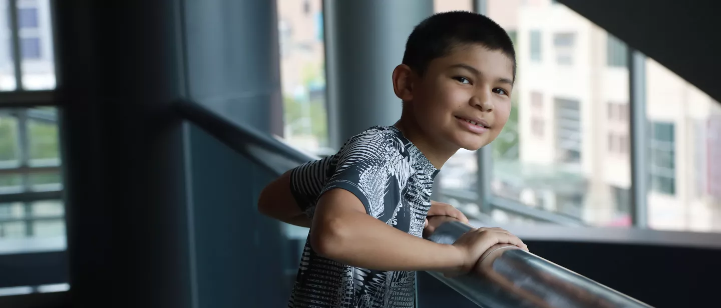 A boy smiling while standing over a railing in a hospital