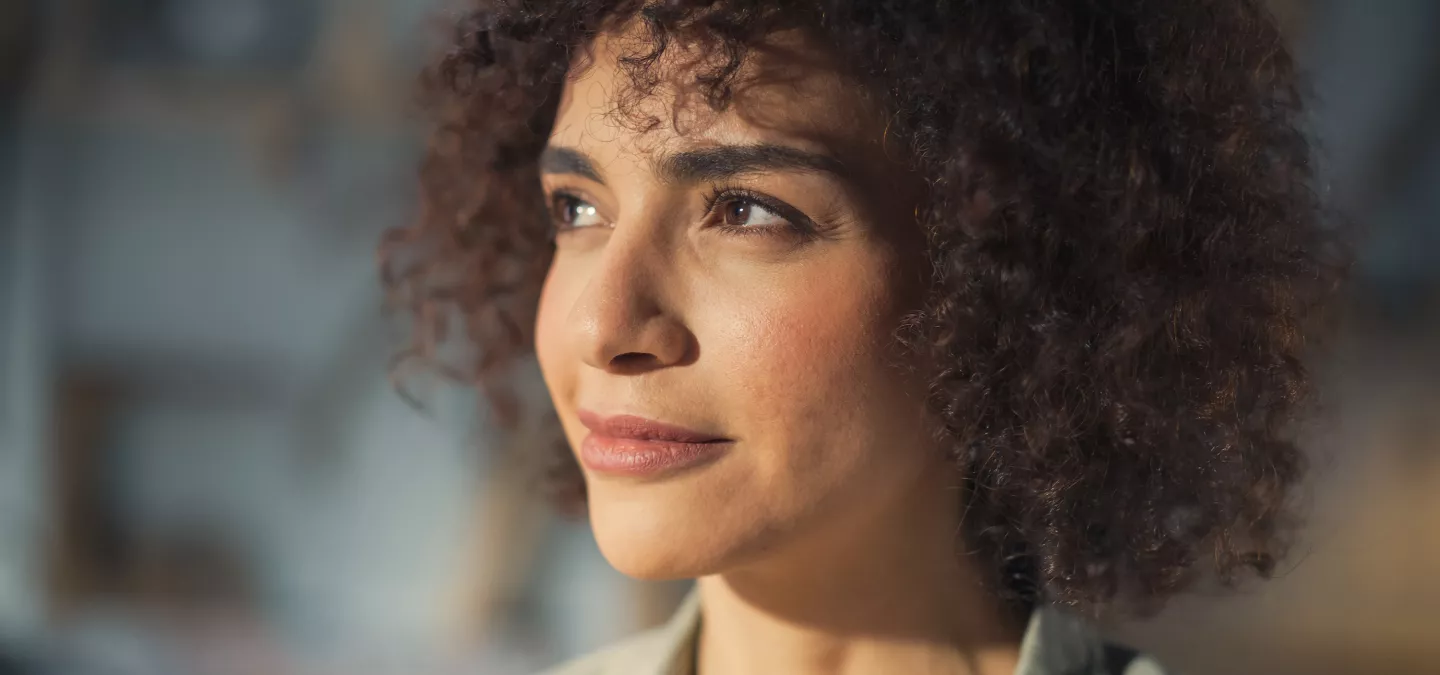 A woman with curly hair looking thoughtfully into the distance with soft lighting.