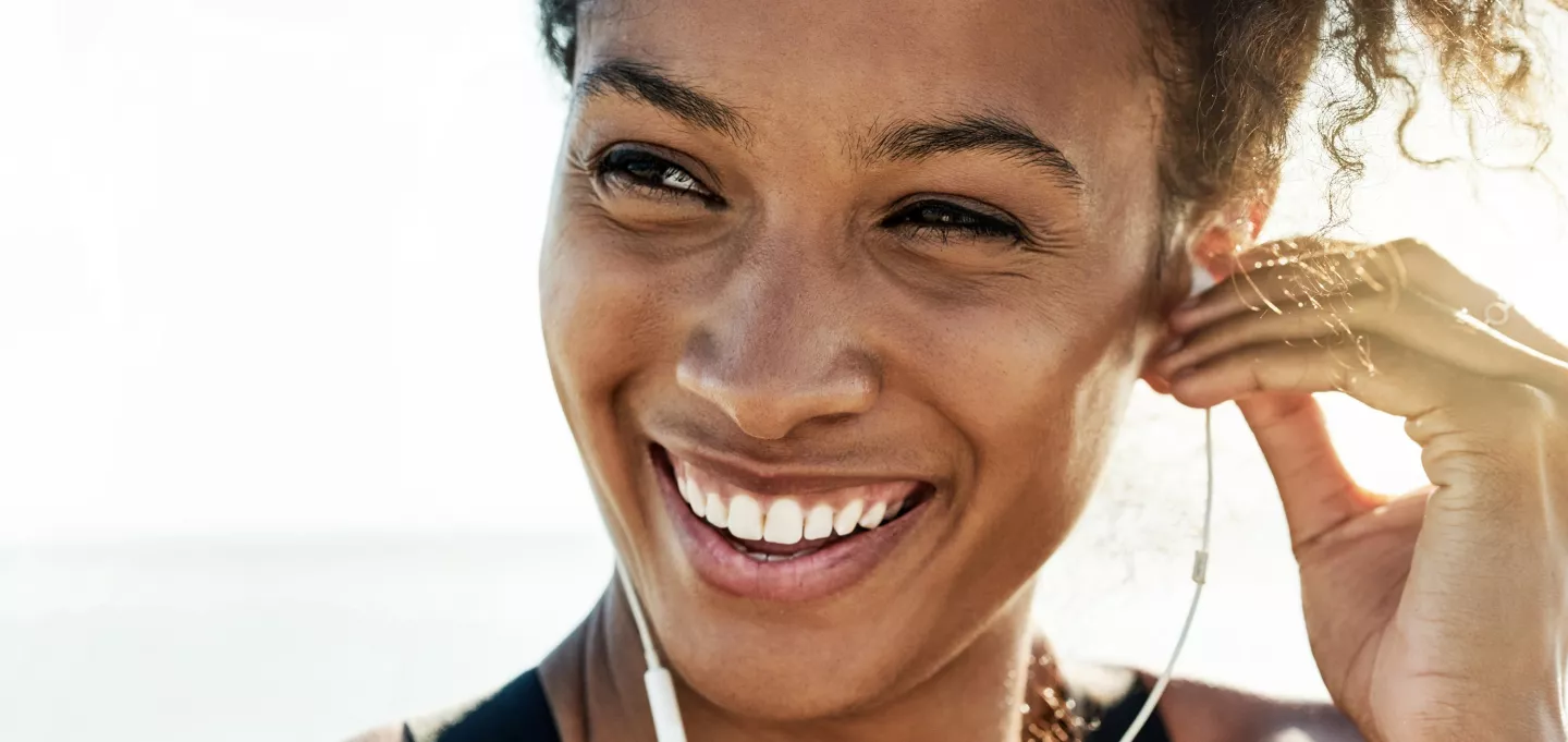 A woman putting in an earbud while smiling on the beach