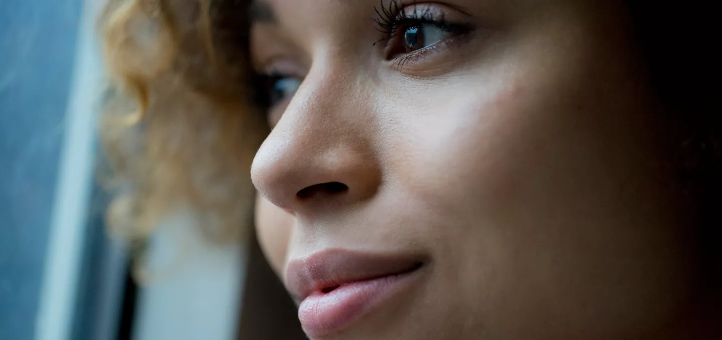 Close-up of a thoughtful woman with curly hair gazing out a window, soft natural light highlighting her serene expression.