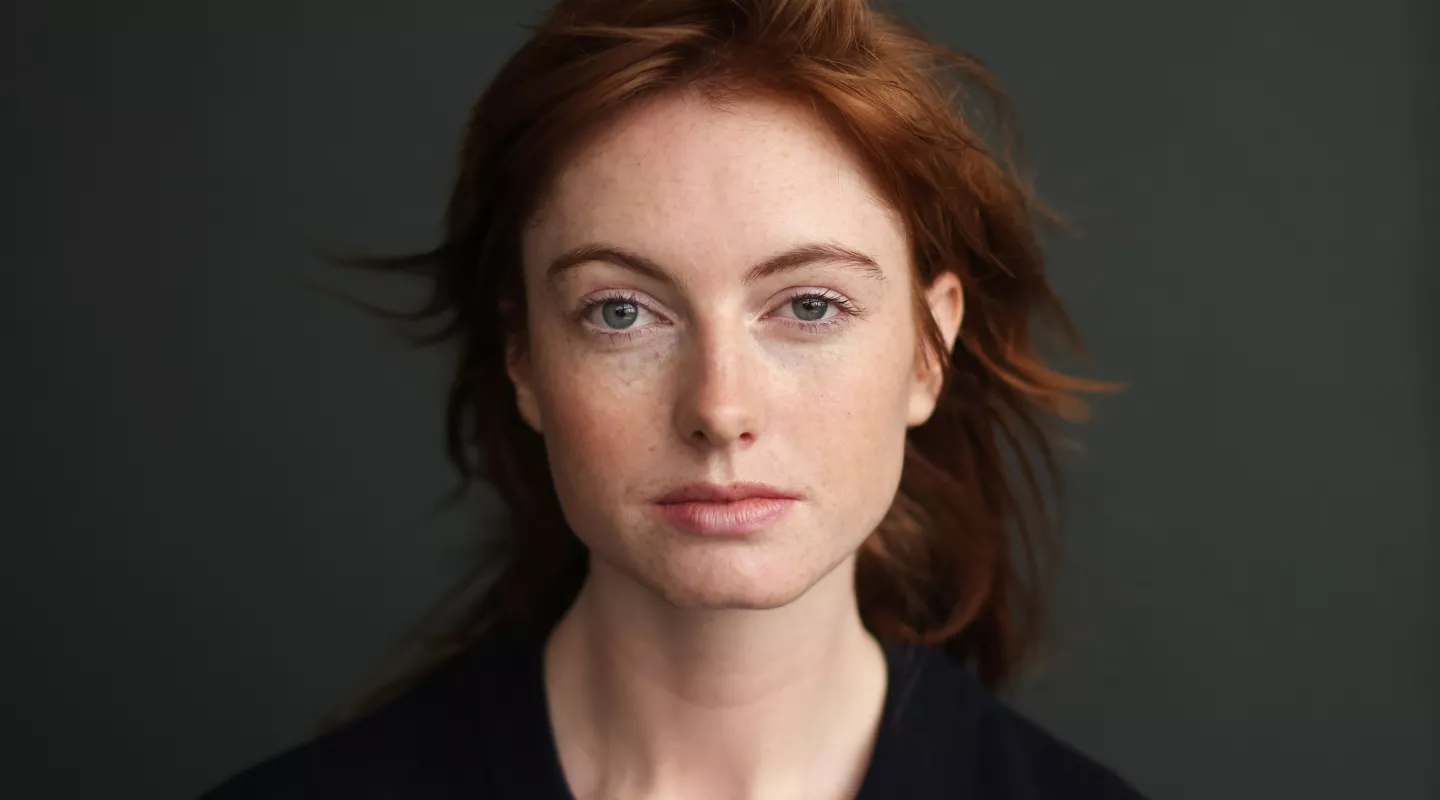 Close-up portrait of a woman with fair skin and red hair looking directly at the camera with a neutral expression