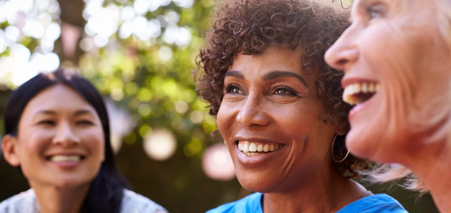 Three women laughing and smiling together outdoors in natural sunlight