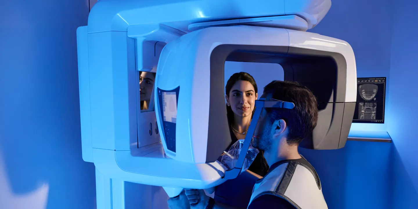 A female medical professional using an X-ray machine to capture images of a male patient.