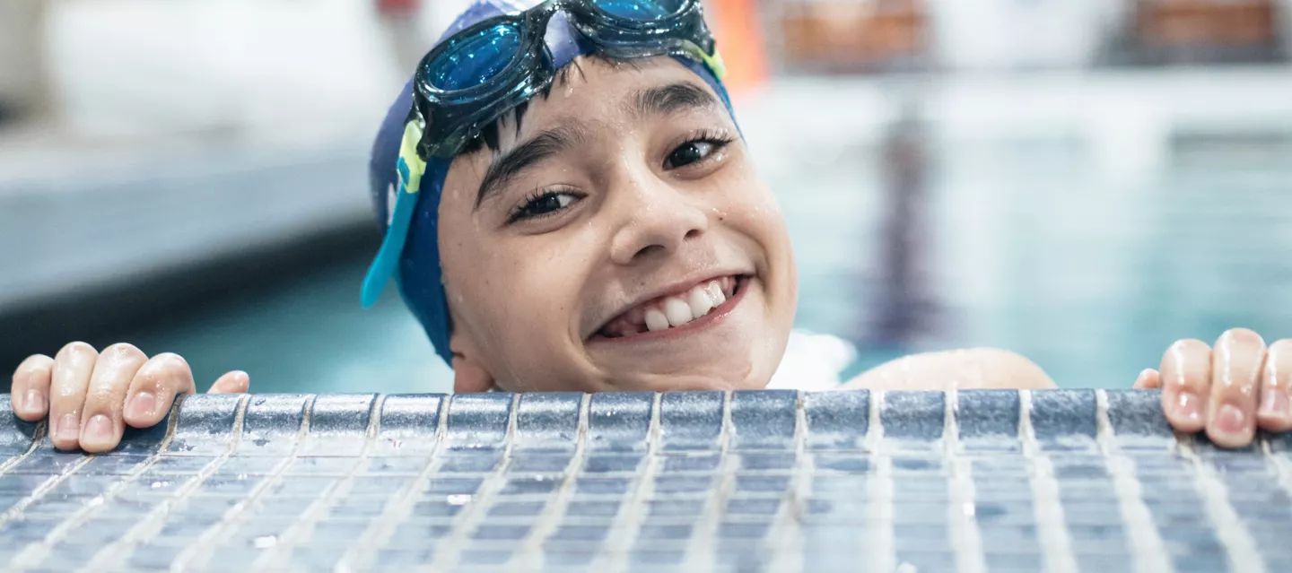 Happy boy in swim goggles smiling at the edge of a pool