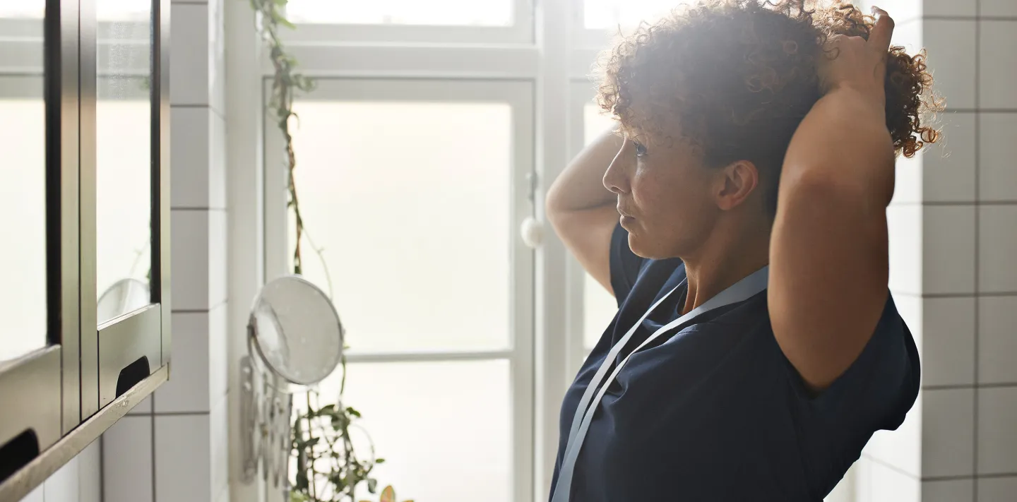 Healthcare worker tying her hair back in a brightly lit room before starting work.