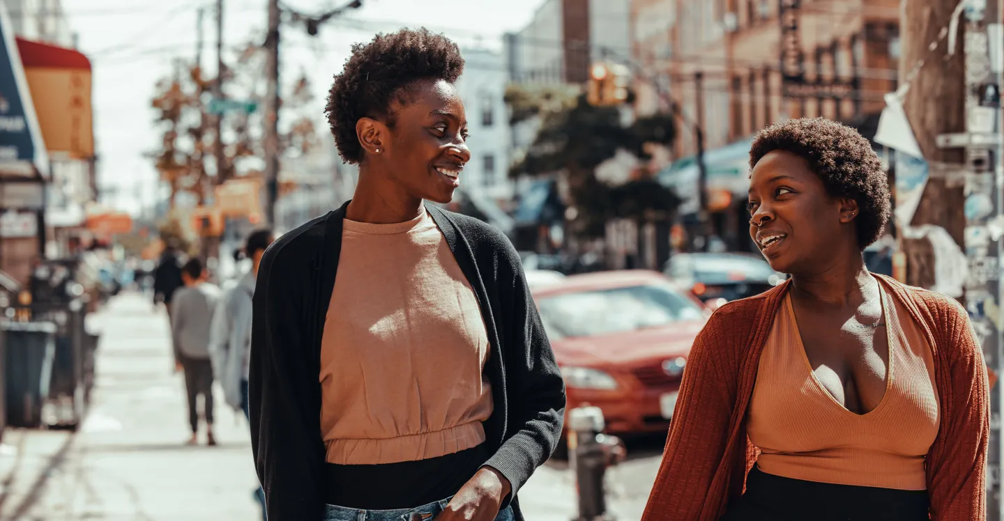 Two friends walking down a city street smiling 