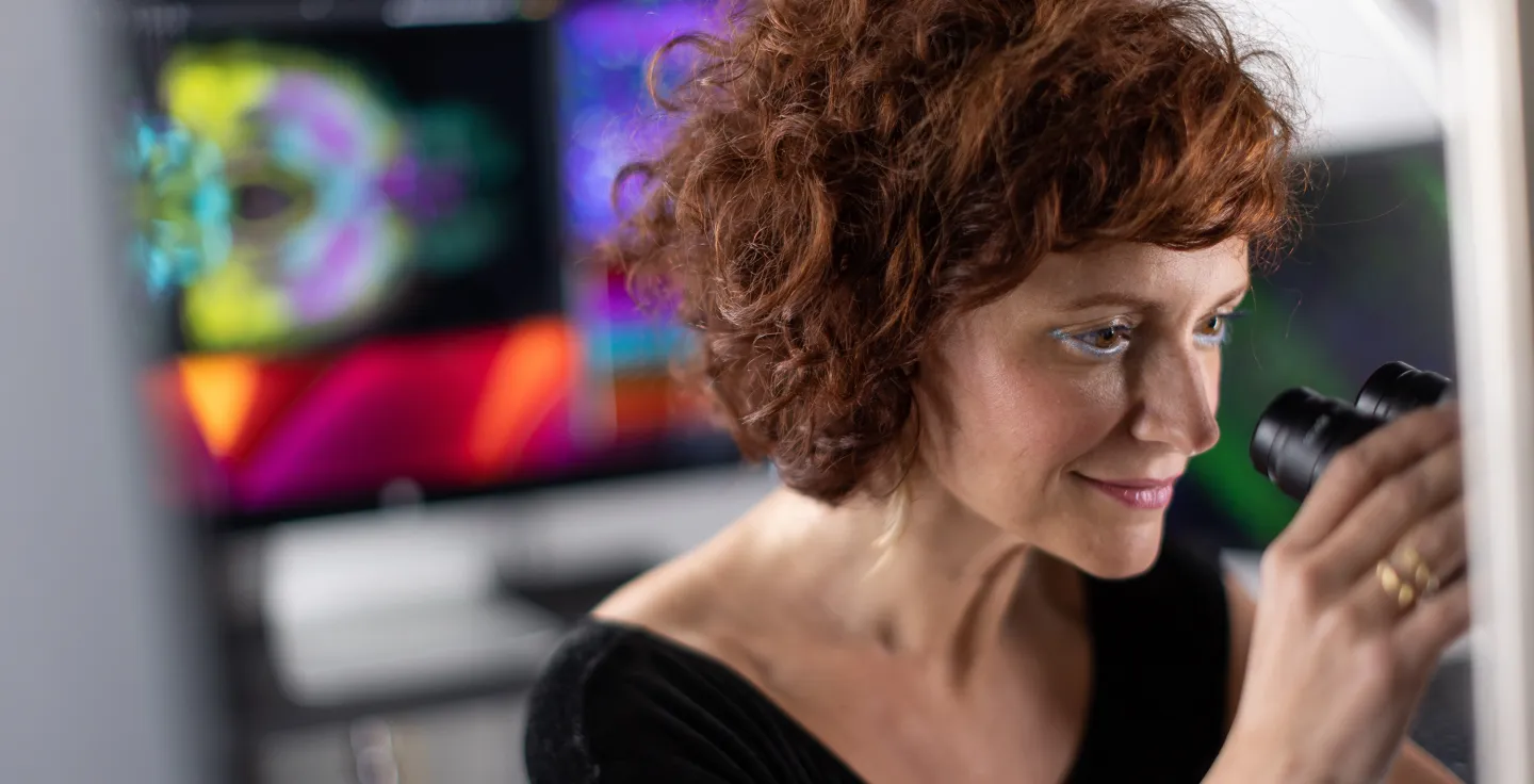 Researcher using a microscope with vibrant imaging displayed on nearby monitors.