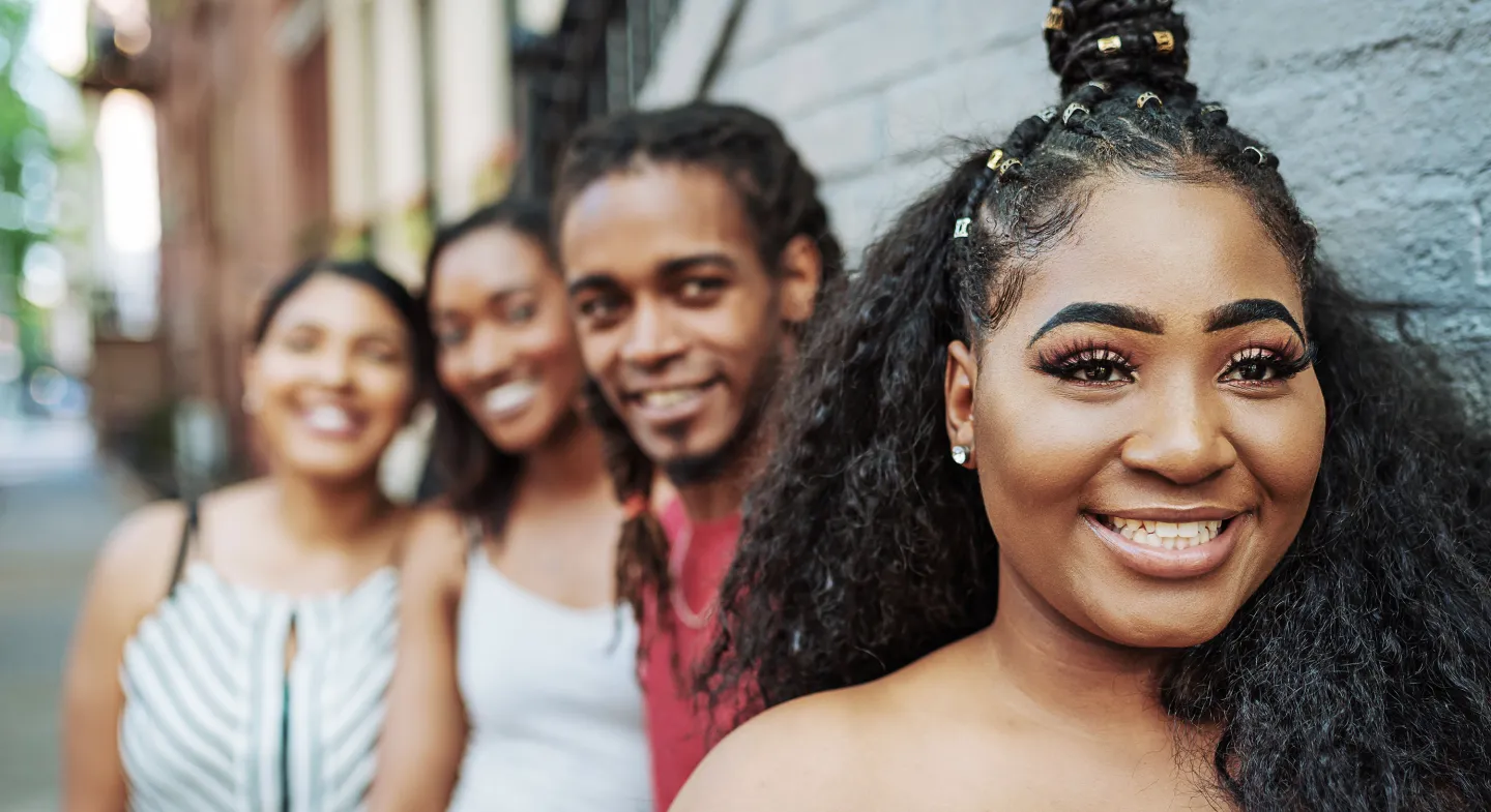 Young woman smiling confidently in focus while standing with three friends on a city sidewalk, all appearing happy and relaxed.