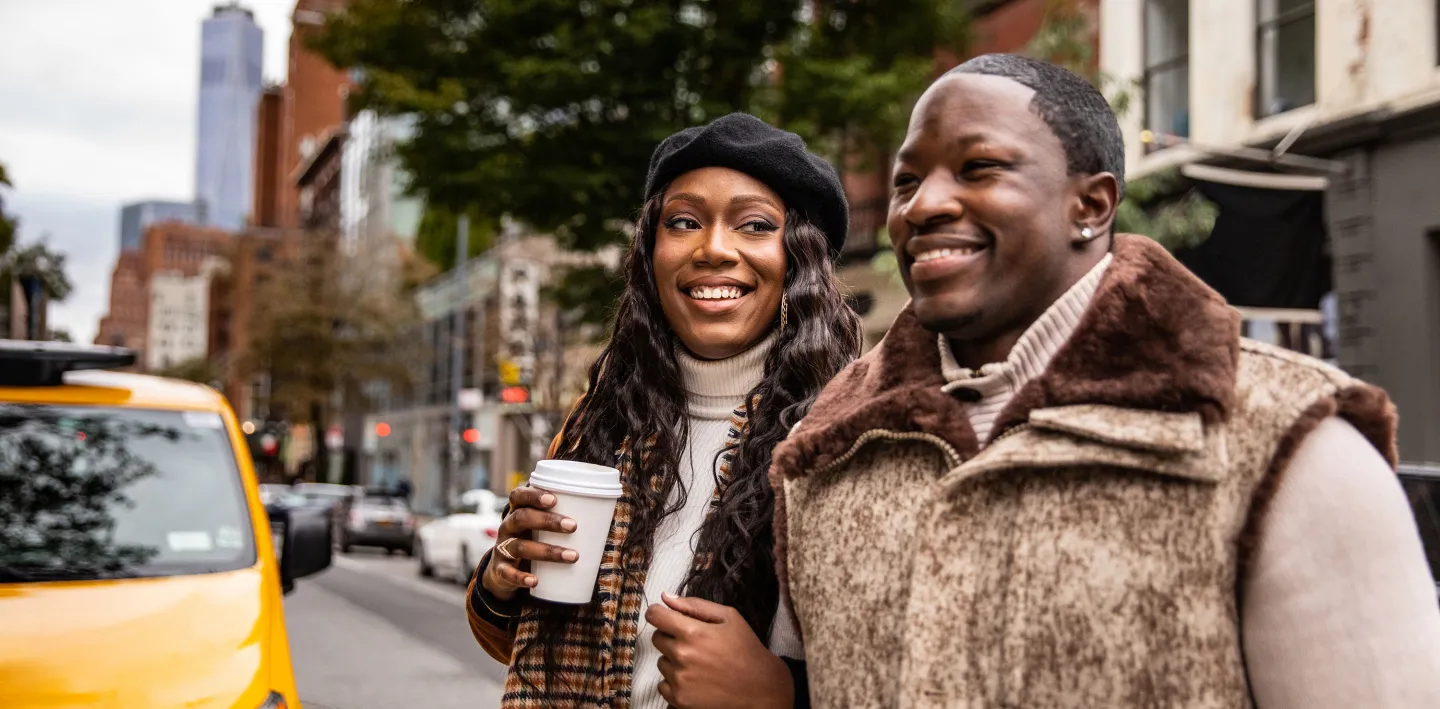 Couple smiling while walking on a city street with coffee and dressed warmly on a chilly day.
