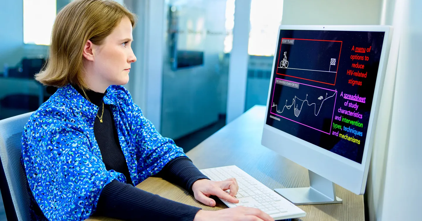 A focused woman in a blue floral shirt views a colorful infographic on HIV stigma reduction on a desktop monitor.