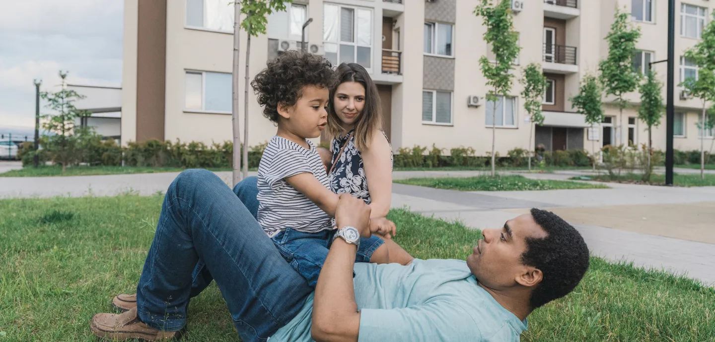 Family of three spending time together on the grass outside an apartment building.