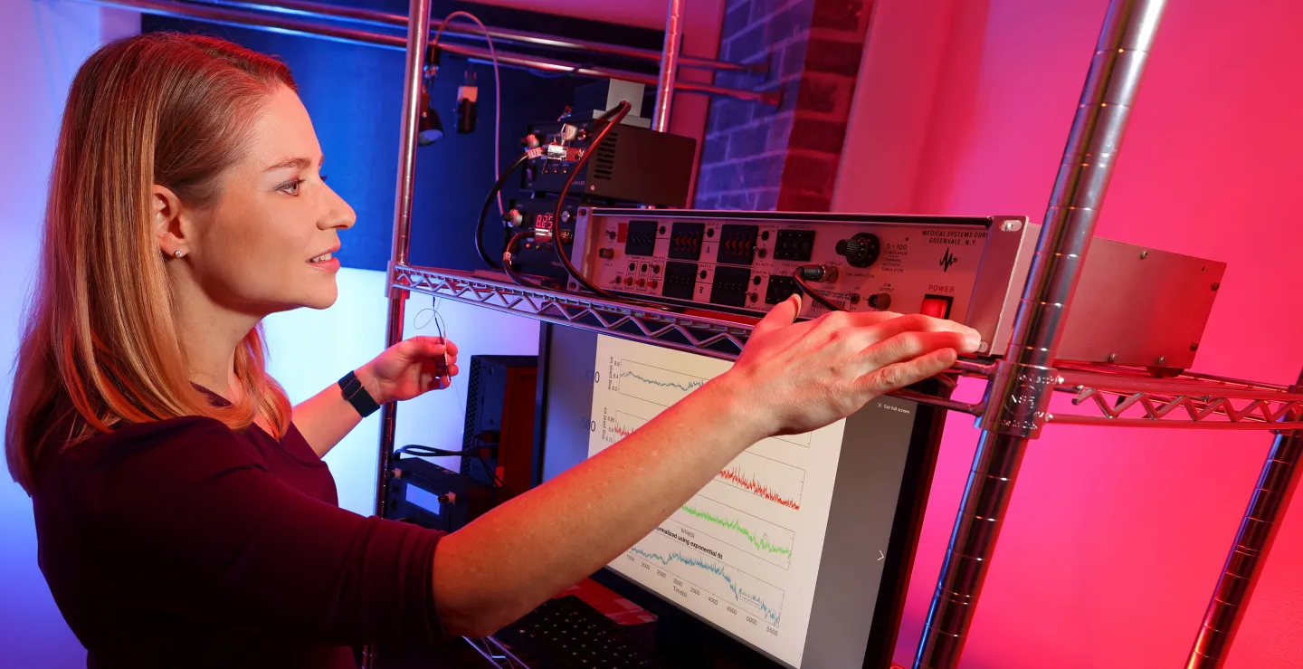 Researcher adjusts lab equipment while monitoring brainwave data on screen under blue and red lighting.