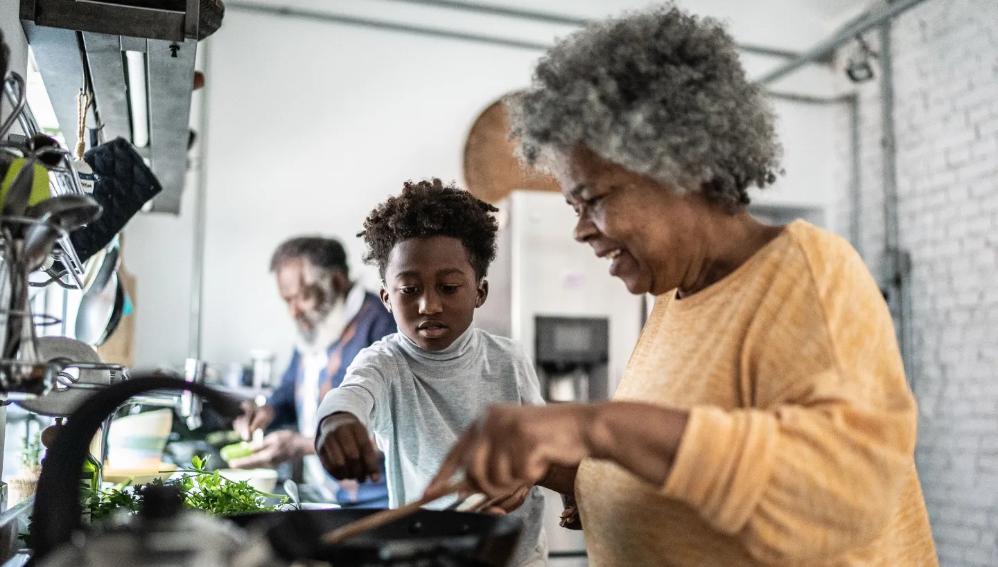 A grandmother and grandson smiling while preparing food together in a home kitchen.