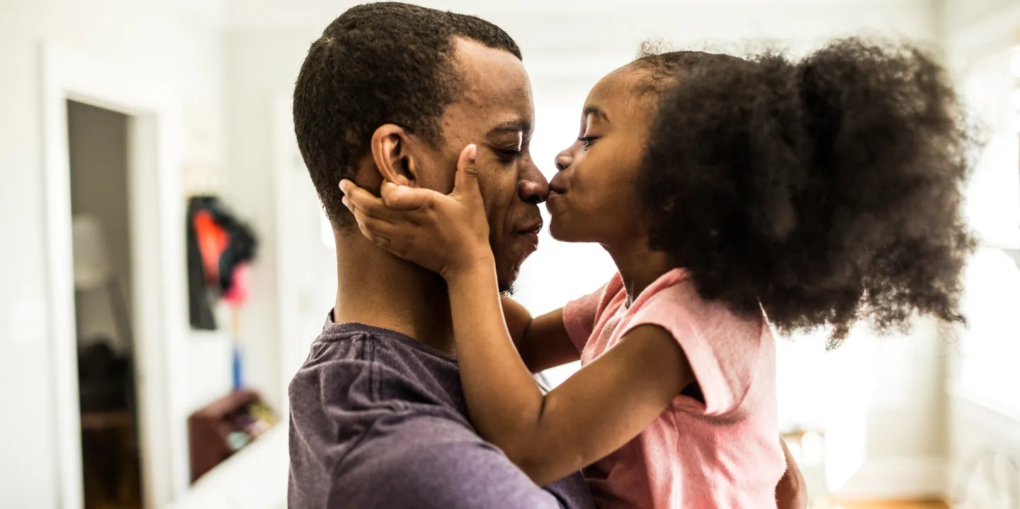 Young girl kisses her father's nose while holding his face lovingly