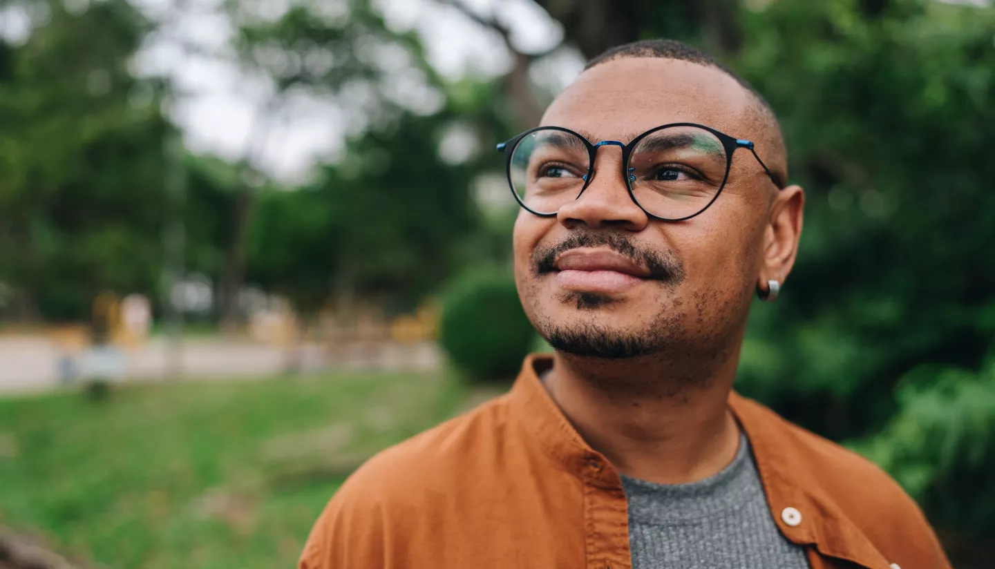 Person in glasses looking thoughtfully in a green park.