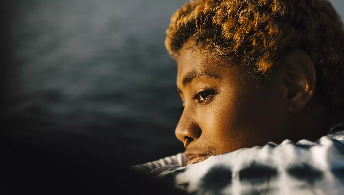 Woman with short hair gazing thoughtfully over a body of water at sunset.
