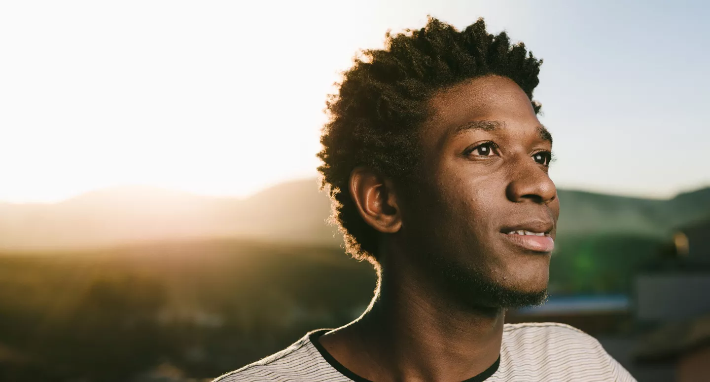 Young man in thoughtful expression looking into distance at sunset