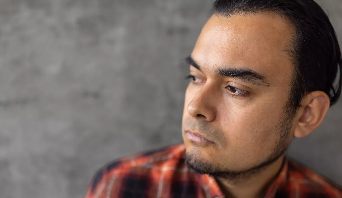 Man in plaid shirt looking thoughtful against a gray wall