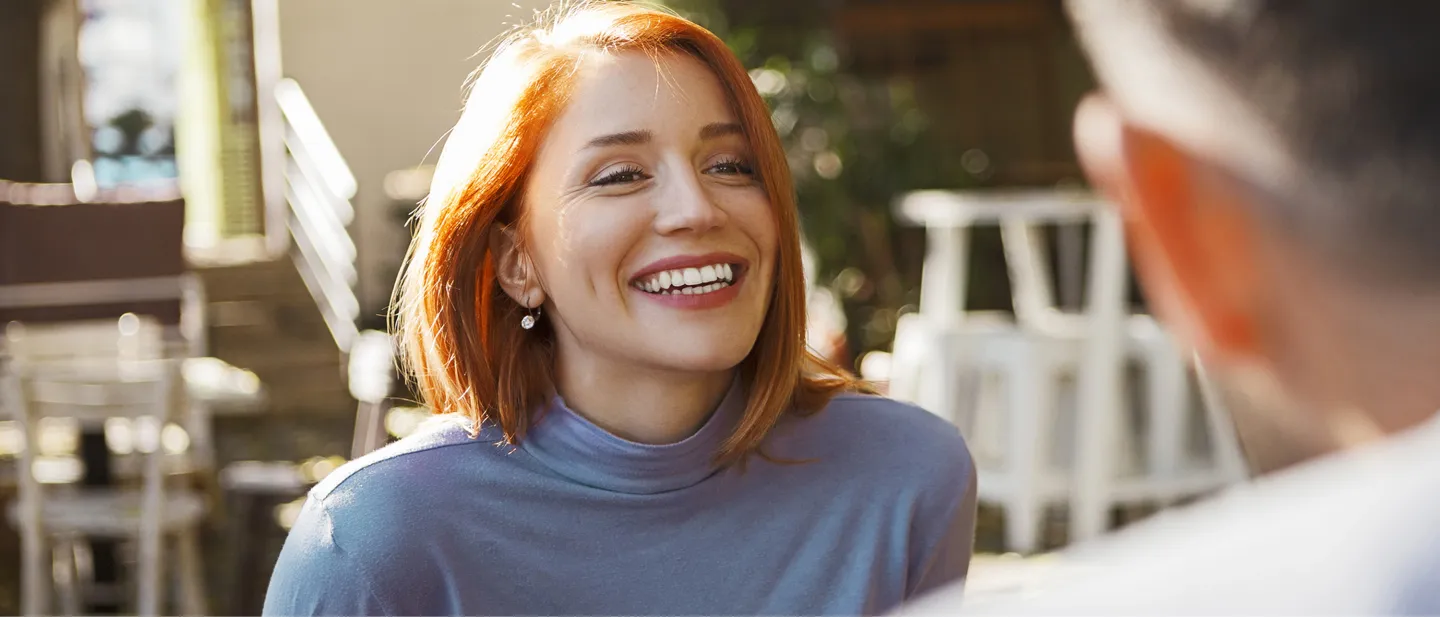 Laughing woman with red hair talking to someone at an outdoor café