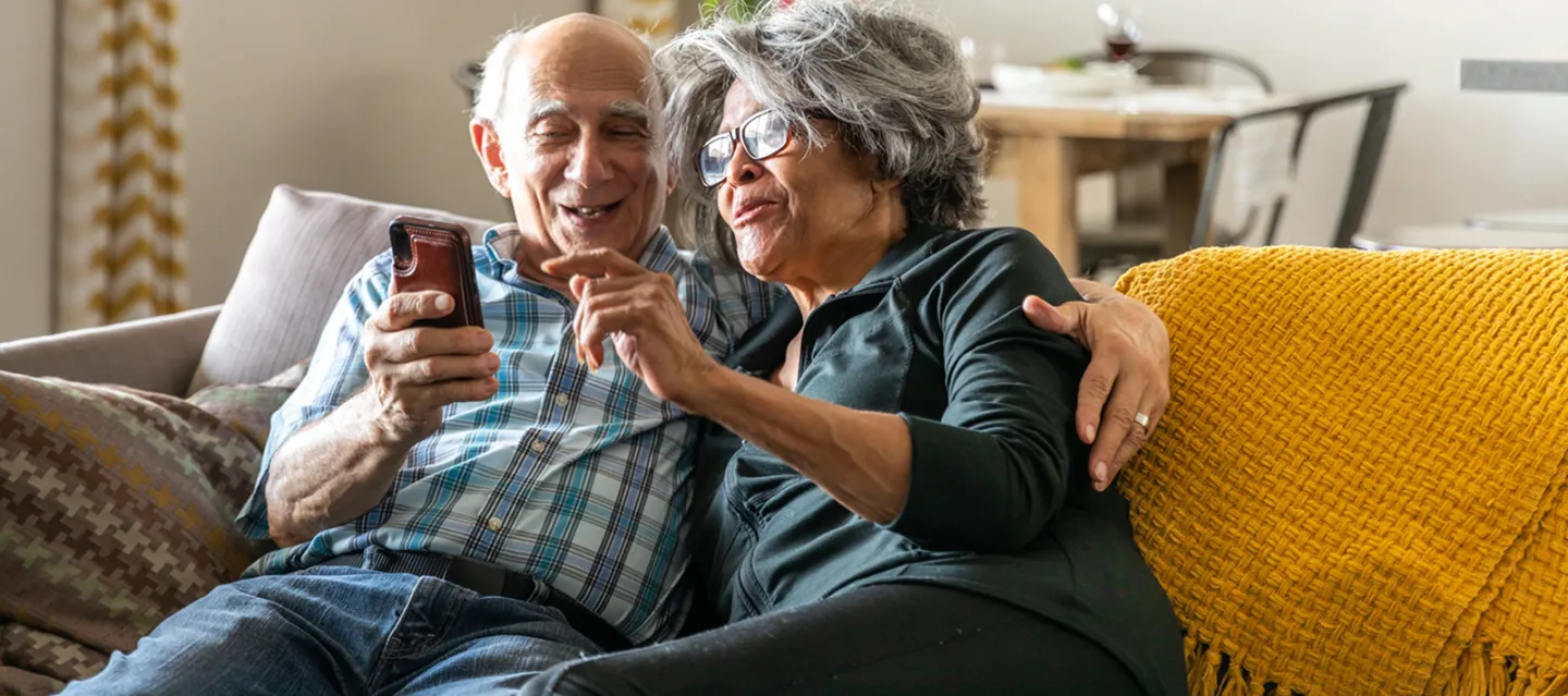 Elderly couple sitting on couch looking at phone