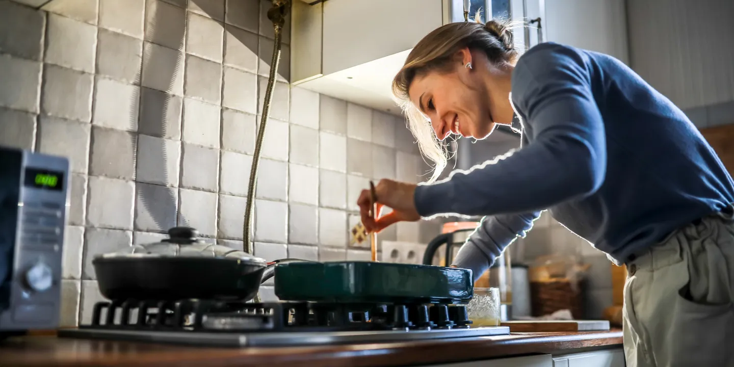 Woman smiling while cooking on a stovetop in a home kitchen.