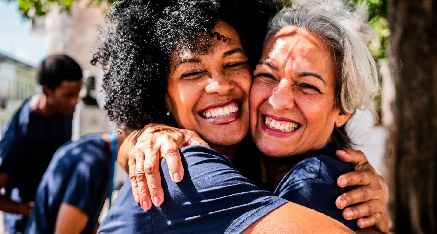 Two women smiling and hugging each other outdoors, radiating joy and warmth.