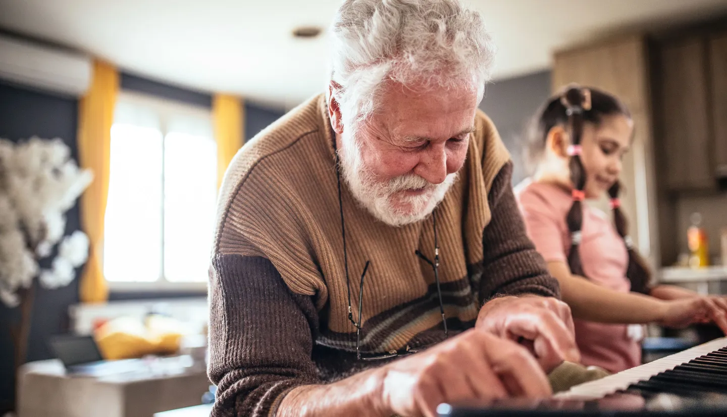 Elderly man and young girl playing piano together in a sunlit room