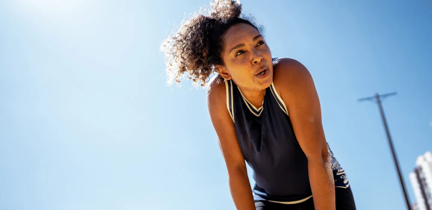 Exhausted woman leaning forward after a workout under bright blue sky