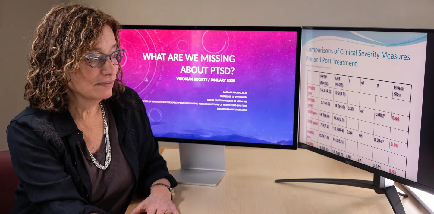 Woman reviewing PTSD research slides on two monitors showing treatment comparison data.