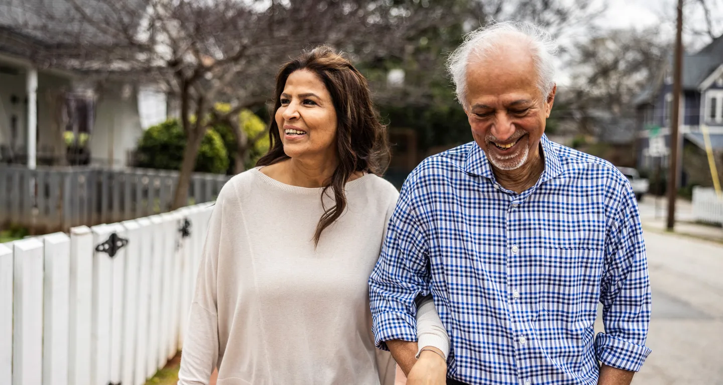 Happy couple walking arm in arm down a residential street on a cloudy day.