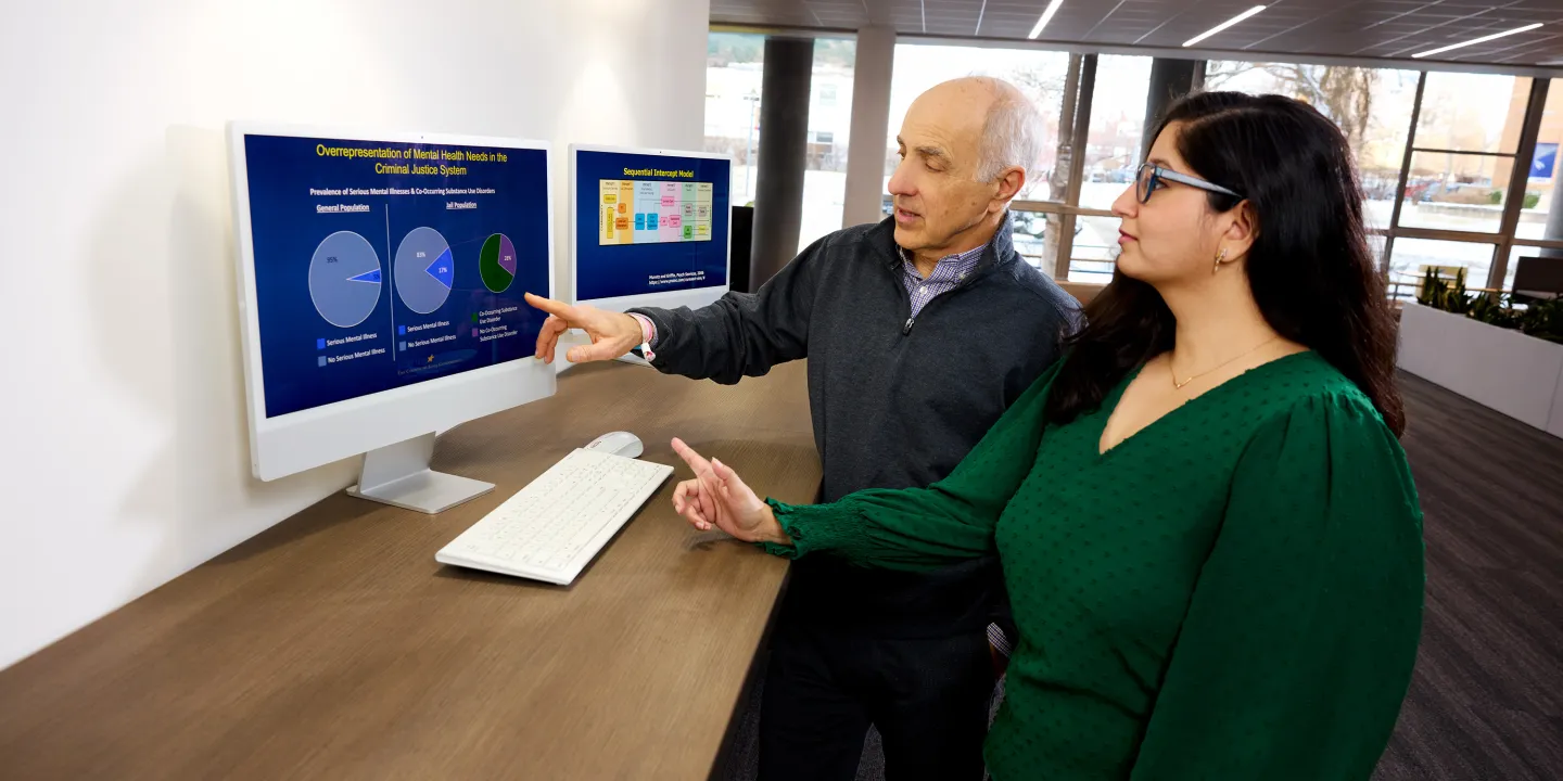 Man and woman reviewing mental health data charts on computer monitors in a bright office setting