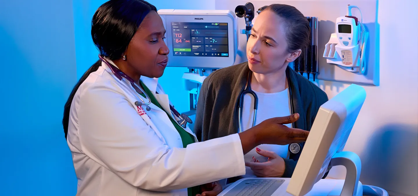  Two healthcare professionals review medical information on a monitor in a clinical exam room.