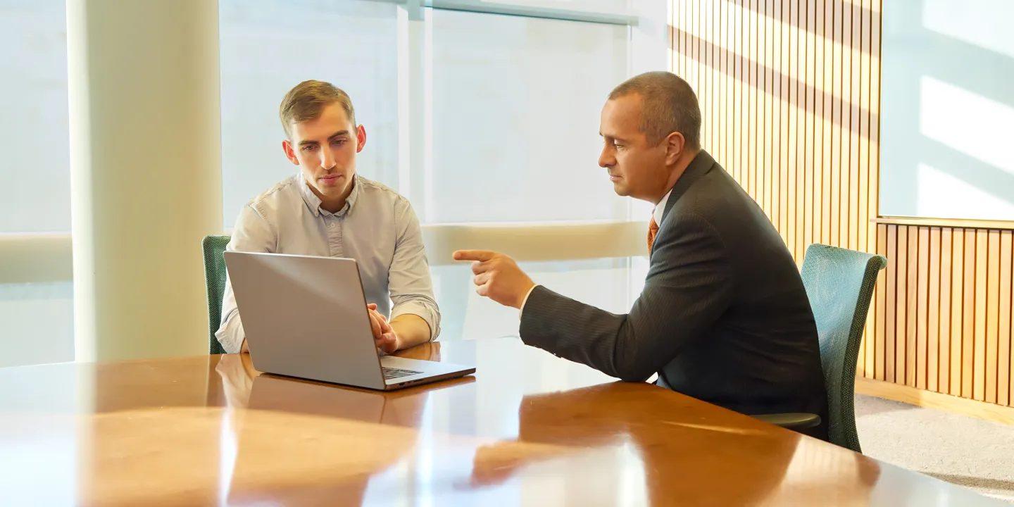 Two men in conversation looking at a laptop in a modern office setting.