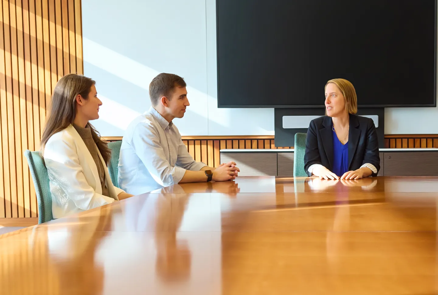 Three professionals seated at a conference table engaged in a discussion in a modern meeting room.