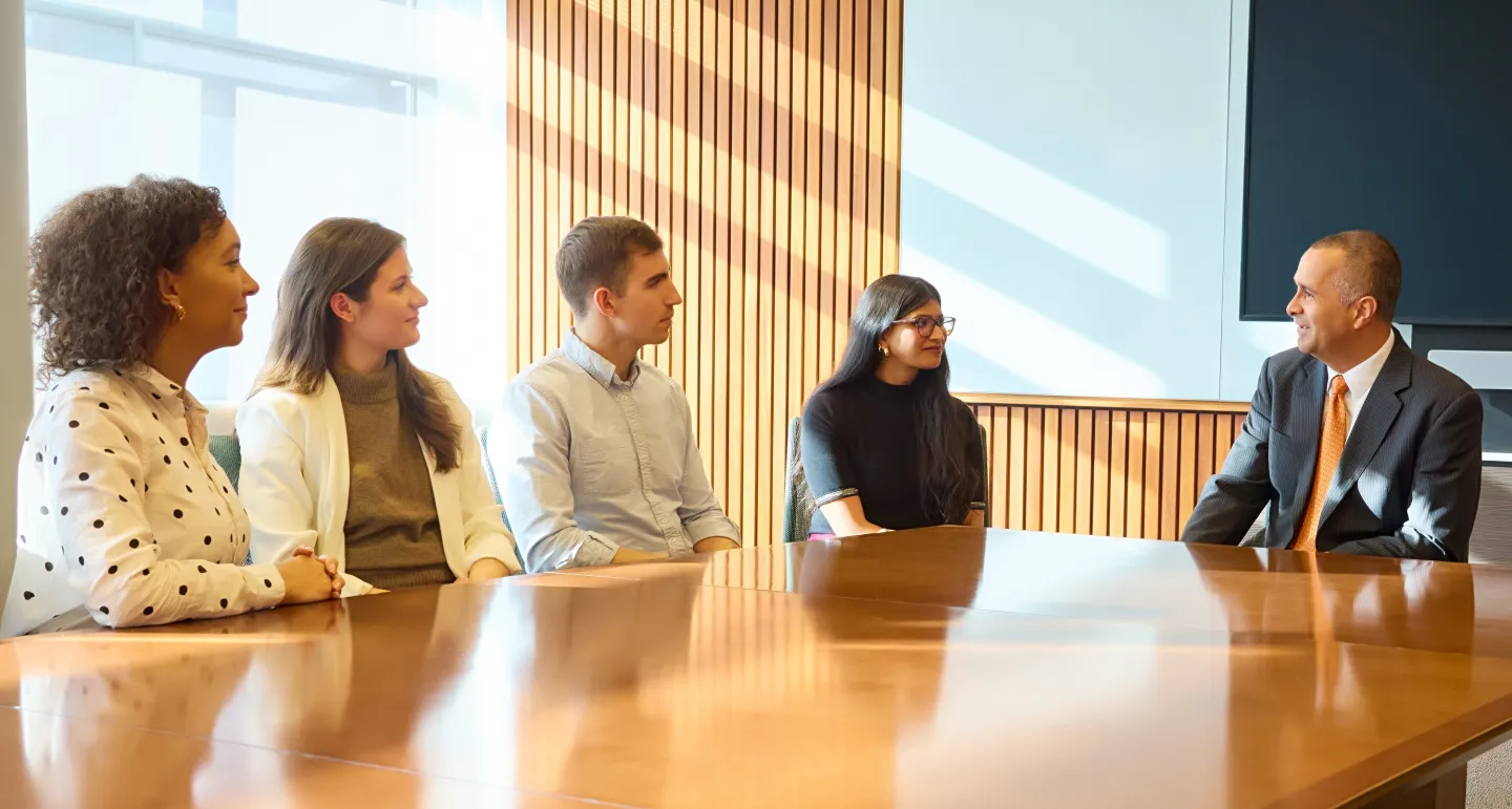 Two young professionals and a man in a suit seated around a conference table engaged in discussion.