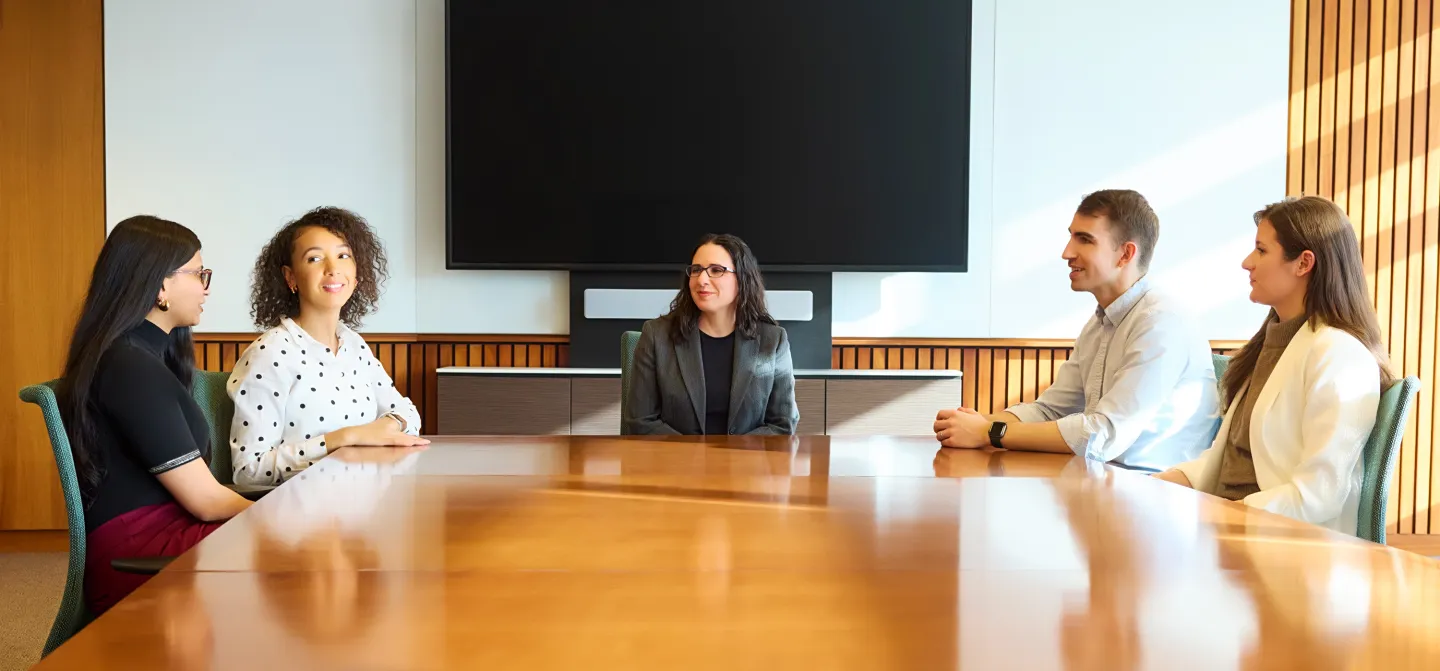 Five people seated around a large conference table having a discussion in a modern meeting room.