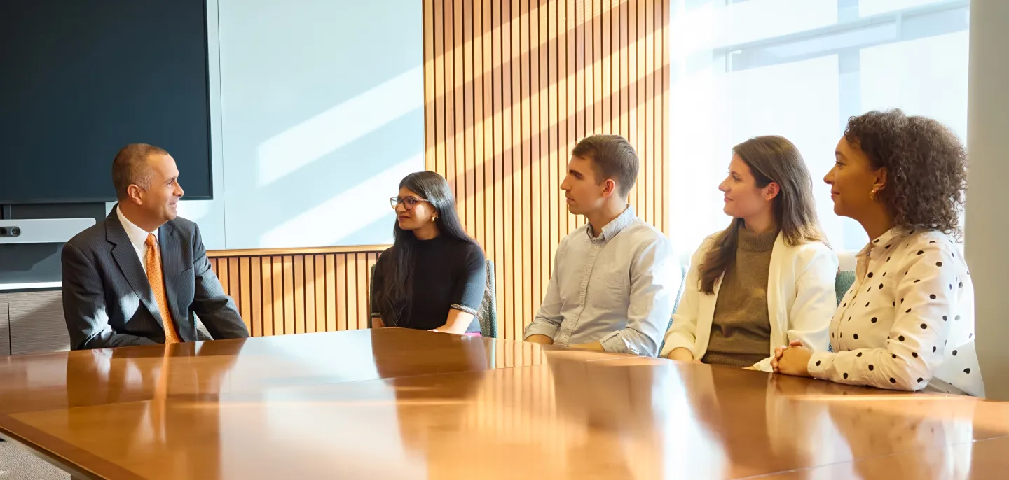 Five people sitting around a conference table having a discussion in a brightly lit room
