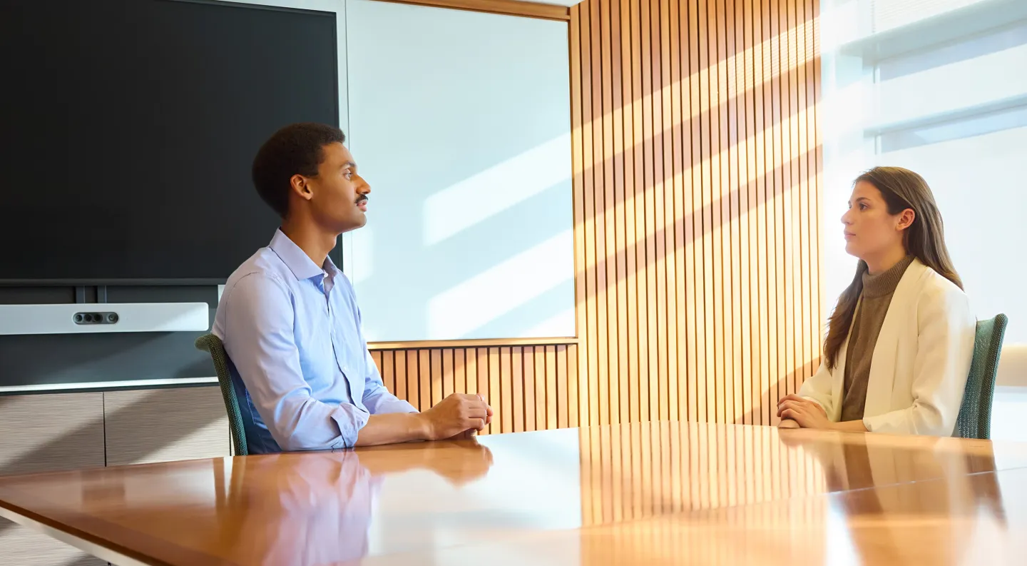 Two professionals seated across from each other at a conference table in a sunlit modern office.