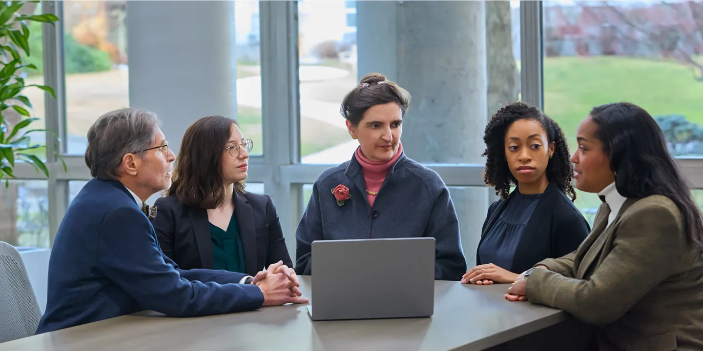 Five professionals in discussion around a laptop during a meeting in a modern office space