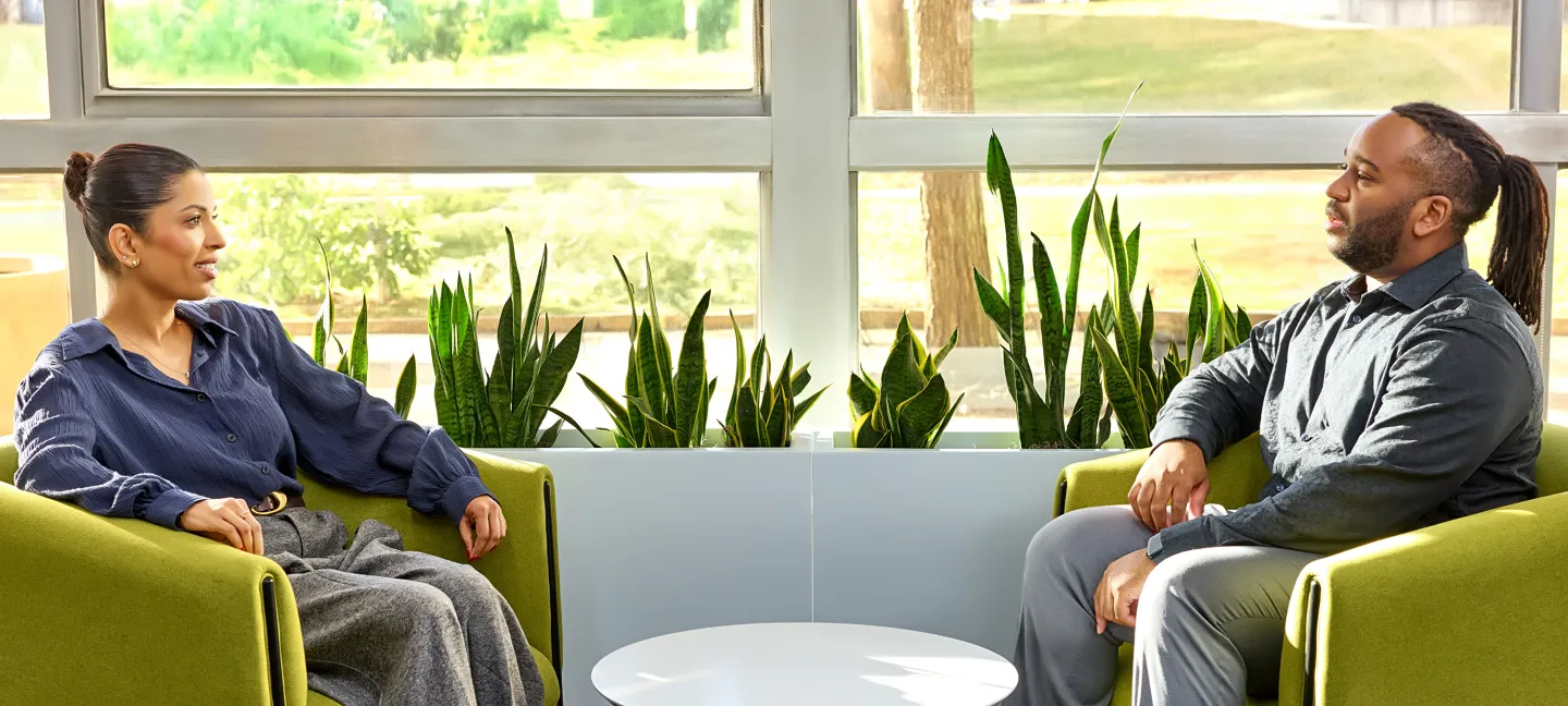 Two colleagues seated in green chairs having a conversation in a sunlit room with plants
